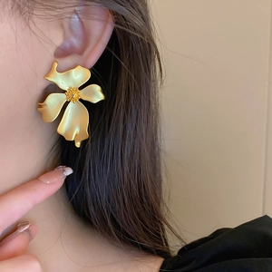 Close-up of golden floral stud earrings with matte metal finish worn by a model