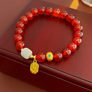 Détail du bracelet à perles rouges avec breloque dorée Fu et perle cylindrique en jade blanc