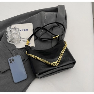 Detail of black quilted leather shoulder bag with gold chain strap on grey blazer background