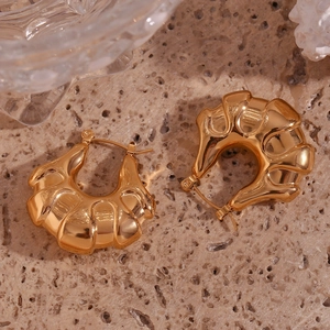 Macro detail of 18K gold plated hoop earrings with textured wavy surface on stone background