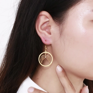 Macro shot of gold angel wing drop earring featuring a crystal stone on female model