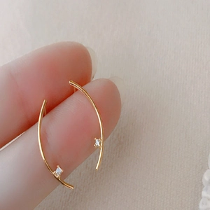 Minimalist gold curved stud earrings with small zircons held by fingers for scale