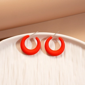 Detail of red acrylic C-shaped earrings with silver pins on a white ceramic plate