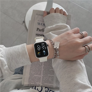 Close-up of a white digital watch with a silver fitness charm bracelet on wrist