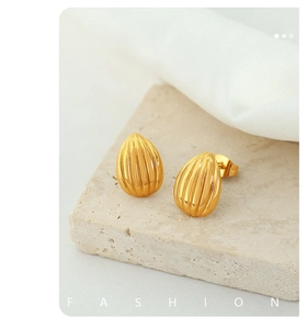 Macro shot of gold teardrop earrings with ribbed texture on a natural stone block