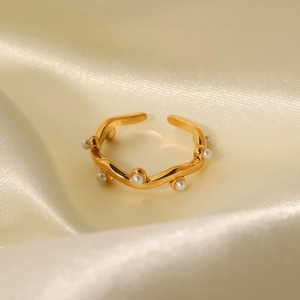 Detail of 18K gold plated wavy ring with white pearls on a soft beige silk background