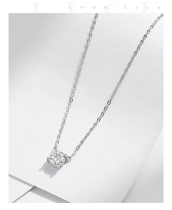 Close-up of a silver four-prong moissanite pendant on a fine chain over white paper