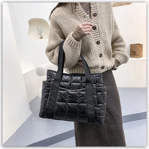 Detail of a black quilted tote bag with padded down-jacket texture and side pockets