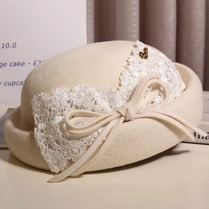 Detail of cream wool cloche hat featuring lace floral embroidery and bow with gold heart charm