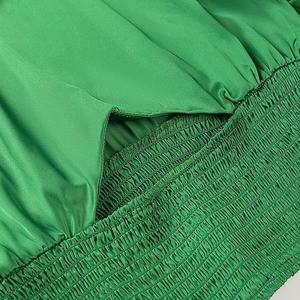 Detailed macro view of vibrant green satin fabric with smocking texture on woman top