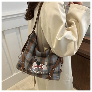 Model wearing a plaid fabric shoulder bag with cartoon print in a bright indoor setting
