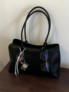 Detailansicht der schwarzen Ledertasche mit Sportanhängern und einer modischen Brille