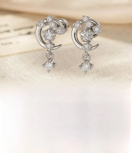 Macro detail of silver star and moon stud earring featuring a small zircon drop