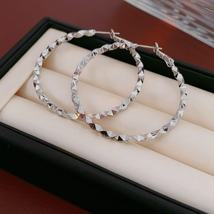 Macro shot of silver textured hoop earrings with diamond-cut pattern in a beige jewelry box