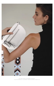 Close-up of a white half-moon chest bag with wide geometric pattern woven strap