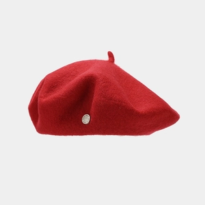Close-up of a red wool beret with a decorative metal badge and classic French style
