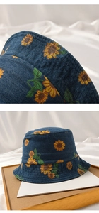 Detail of blue denim bucket hat with sunflower print on a wooden tray with soft lighting