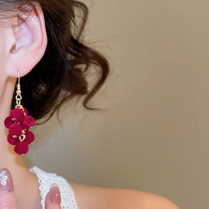 Close-up of deep red flocked grape tassel earring worn by a model in soft lighting