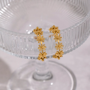 Detailansicht der goldfarbenen C-förmigen Blumenohrringe an einem eleganten Glasrand