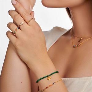 Close-up of elegant gold flower rings with colorful diamonds and a beaded clover bracelet
