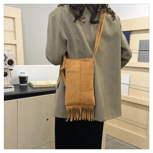 Close-up of a brown suede crossbody bag with long fringes shown on a model