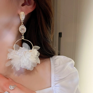 Close-up of elegant gold long drop earrings featuring white petals and sparkling rhinestones
