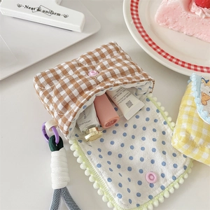 Detail of checkered fabric camera pouch showing plaid cotton texture and plush ball trim