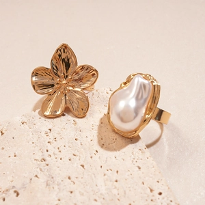 Detailaufnahme von Goldblumenring und Barockperlenring auf einer Natursteinoberfläche