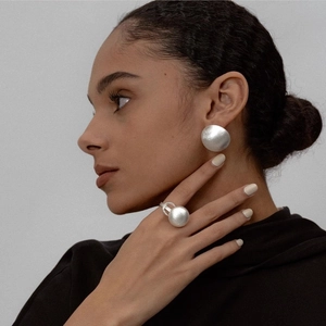Gros plan sur des boucles d'oreilles boules argentées mates et bague sphérique sur modèle
