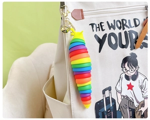 Rainbow-colored fidget slug keychain with golden clasp and bell on white backpack zipper