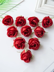 Top view of ten red silk artificial rose heads with green sepals on a white desk