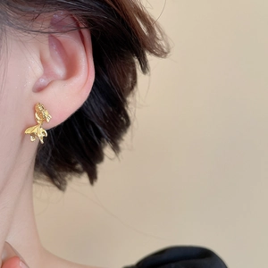 Detailed view of goldfish shaped gold earrings with scales on female model ear