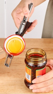 Macro shot of stainless steel jar opener tool loosening a red lid on glass jar