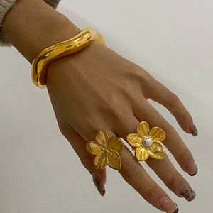 Close-up of gold wave bracelet and flower ring with pearl on woman's hand