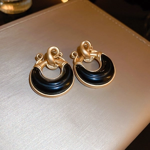 Macro detail of vintage gold C-shaped earrings with black resin inlay and knotted design
