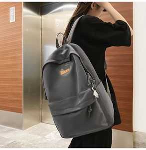 Dark grey backpack with astronaut charm shown on a model against a modern wall