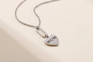 Detailed close-up of a silver heart pendant with MOM engraving on a textured background