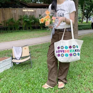 Close-up of floral embroidery on a cream canvas tote bag in an outdoor setting
