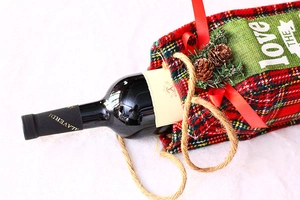 Detail of red and green plaid fabric wine gift bag with pine cone and burlap handle