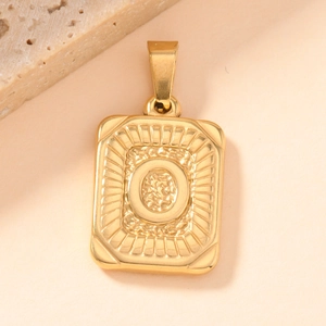 Macro detail of gold-plated rectangular charm with engraved letter O and sunburst pattern