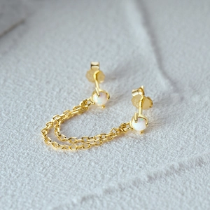 Macro shot of S925 silver gold-plated opal chain stud earrings on stone texture