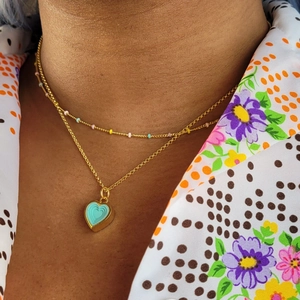 Gold double-layer necklace with colorful beads and a blue heart pendant worn by model