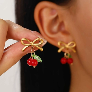 Detail shot of a model wearing golden bow earrings with red cherries and green leaves