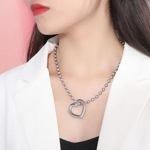 Silver hollow heart pendant necklace with bead chain on model against pink background