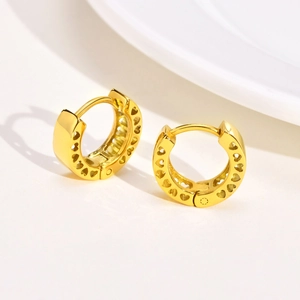 Detailed view of gold huggie earrings featuring delicate hollowed heart cut-outs