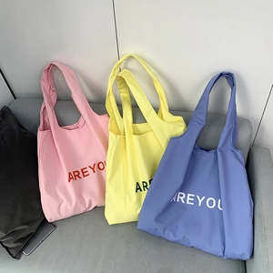 Three large canvas tote bags in pink, yellow, and blue colors on a grey sofa