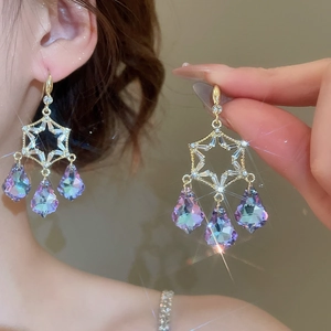 Close-up of golden star-shaped earrings with purple crystal teardrop charms