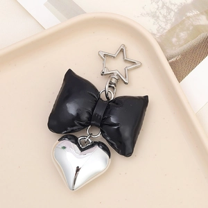 Detail of a black faux leather bow keychain with a silver heart pendant and star-shaped clip