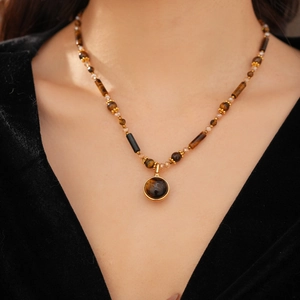 Close-up of a gold necklace with tiger eye stone beads and a large round pendant on neck