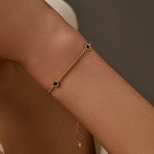 Pulsera minimalista de oro con circonitas verde esmeralda puesta en la muñeca